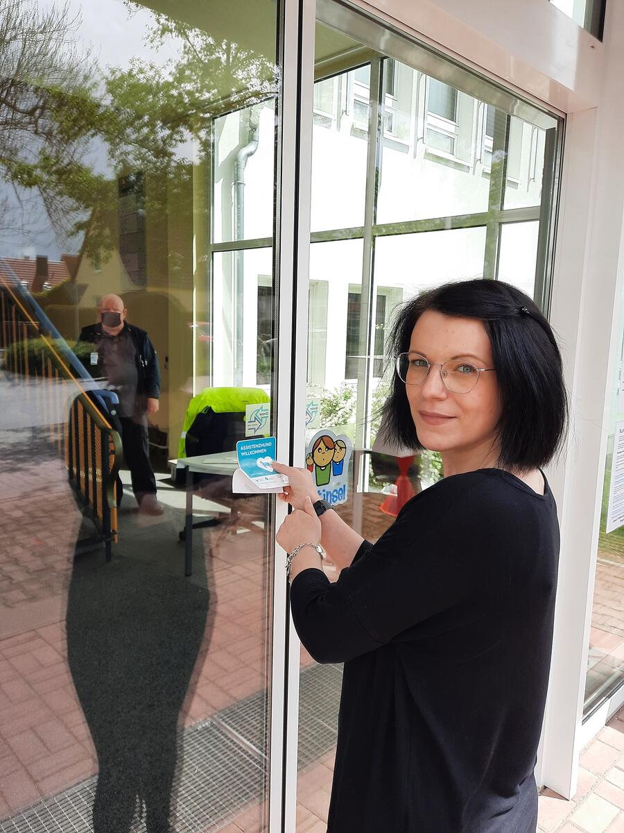 Ramona Fricke bringt den Aufkleber f&uuml;r die assistenzhundfreundliche Beh&ouml;rde am Eingang des Jobcenters in Ilmenau an.